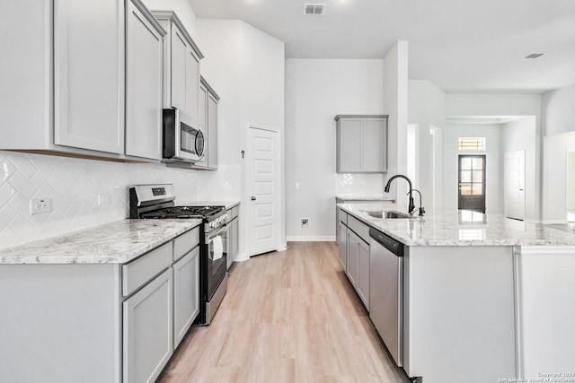 kitchen featuring gray cabinetry, light stone countertops, sink, stainless steel appliances, and light wood-type flooring