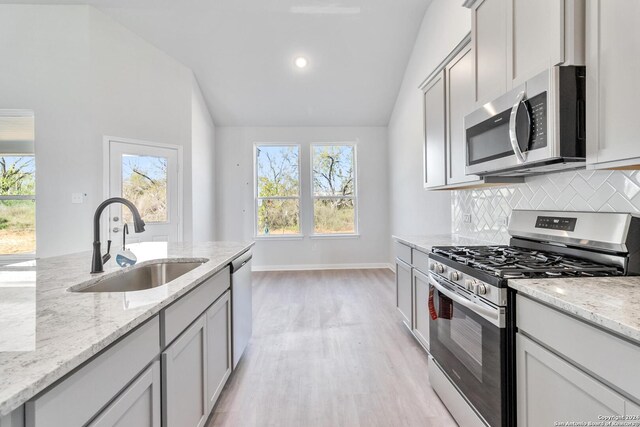 kitchen featuring gray cabinetry, light stone countertops, sink, vaulted ceiling, and appliances with stainless steel finishes