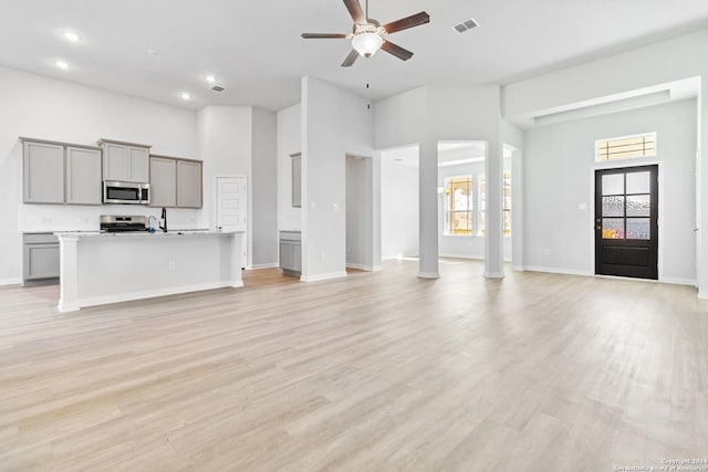 unfurnished living room with ceiling fan, light hardwood / wood-style floors, sink, and a high ceiling