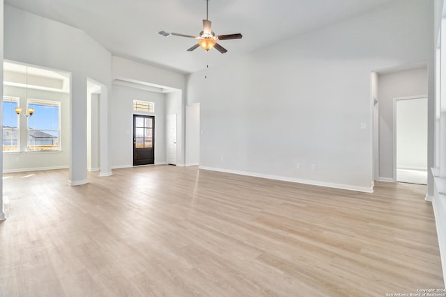 unfurnished living room featuring plenty of natural light, a towering ceiling, ceiling fan with notable chandelier, and light wood-type flooring