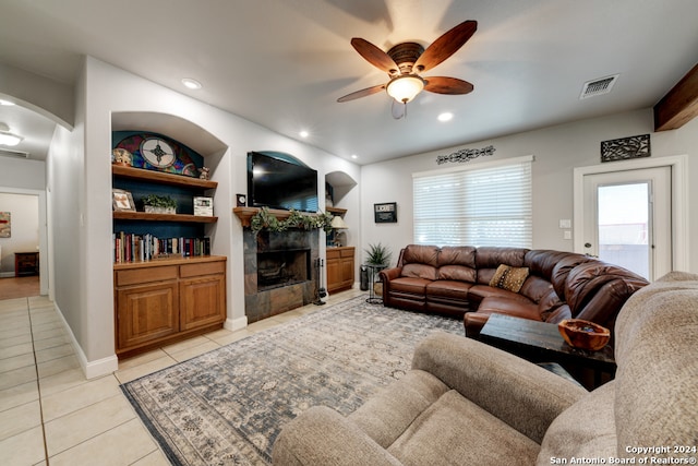 tiled living room featuring a tiled fireplace, built in shelves, and ceiling fan