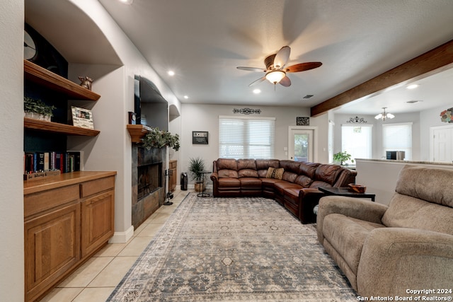 living room featuring beamed ceiling, a tile fireplace, ceiling fan with notable chandelier, and light tile patterned floors