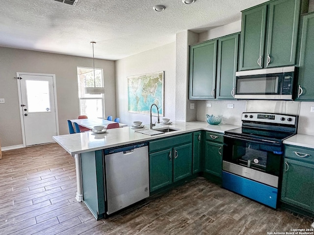 kitchen with pendant lighting, sink, appliances with stainless steel finishes, green cabinetry, and kitchen peninsula