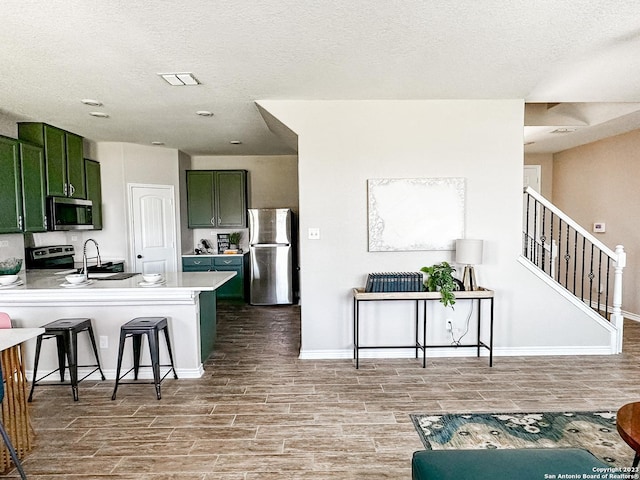 kitchen featuring kitchen peninsula, stainless steel appliances, a kitchen breakfast bar, and green cabinetry