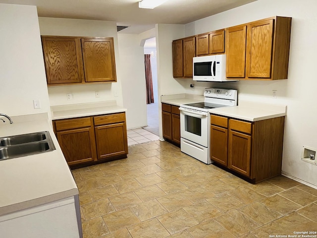 kitchen with arched walkways, white appliances, a sink, light countertops, and brown cabinets