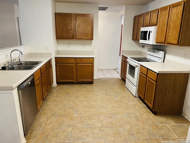 kitchen with brown cabinets, white appliances, visible vents, and a sink