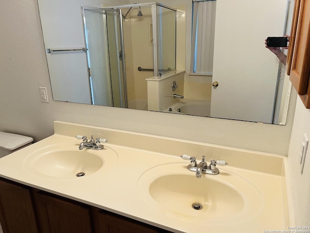 bathroom with a shower with shower door, a sink, toilet, and double vanity