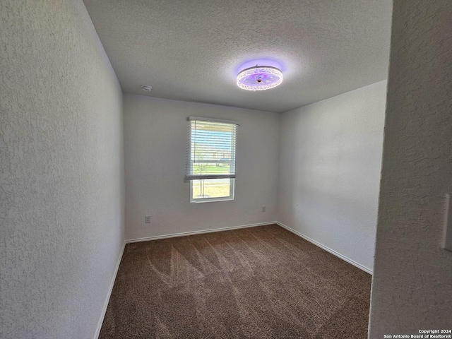 empty room featuring a textured ceiling and dark colored carpet