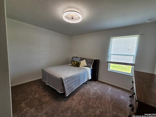 bedroom with a textured ceiling, dark colored carpet, and multiple windows