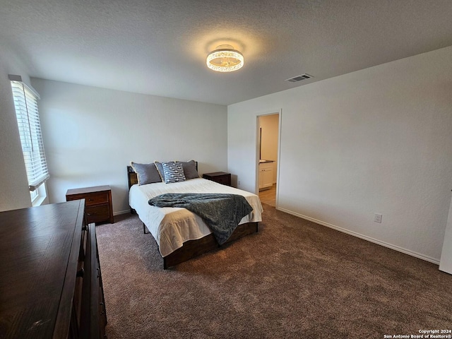 bedroom with a textured ceiling, dark carpet, and ensuite bath