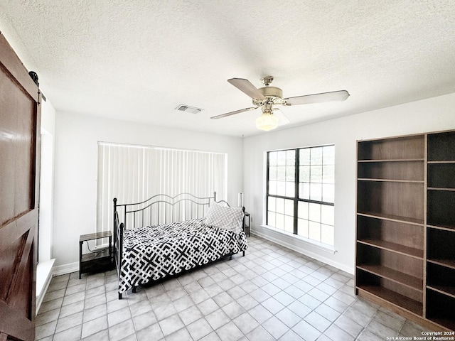 bedroom with a textured ceiling, ceiling fan, and a barn door