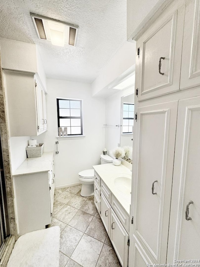 bathroom featuring toilet, a textured ceiling, a wealth of natural light, and vanity