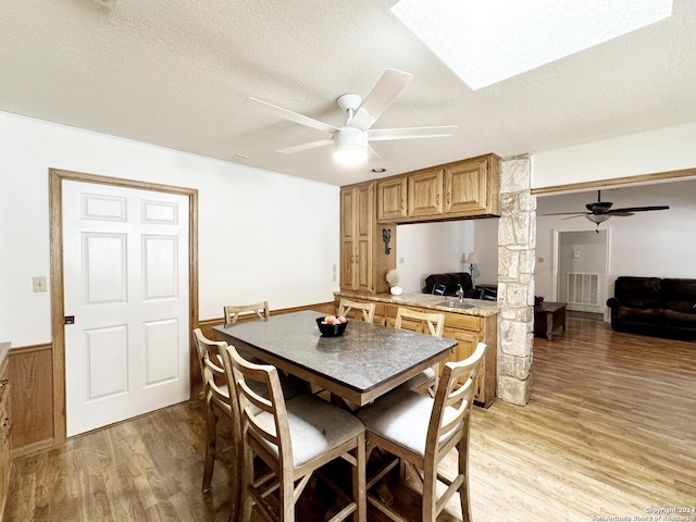 kitchen featuring a textured ceiling, ceiling fan, light hardwood / wood-style floors, and a breakfast bar