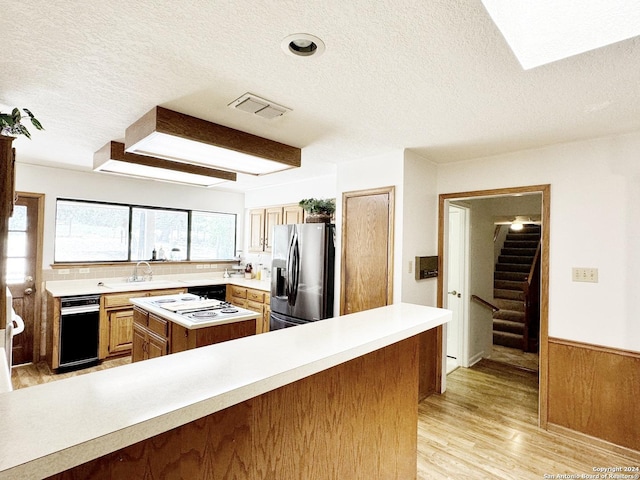 kitchen featuring light hardwood / wood-style floors, wooden walls, stainless steel refrigerator with ice dispenser, a textured ceiling, and sink