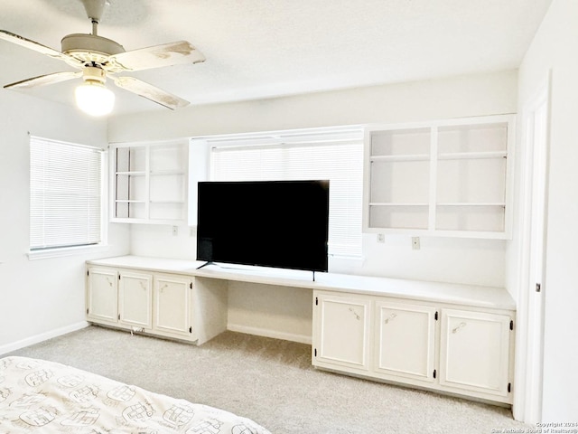 unfurnished bedroom featuring built in desk, ceiling fan, and light colored carpet