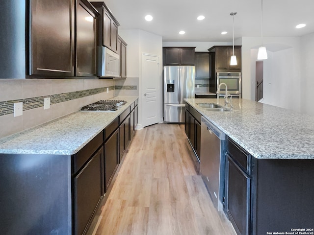 kitchen featuring light hardwood / wood-style flooring, stainless steel appliances, dark brown cabinetry, decorative backsplash, and an island with sink