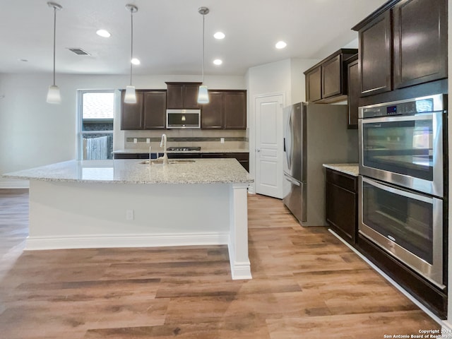 kitchen with light hardwood / wood-style floors, appliances with stainless steel finishes, dark brown cabinets, and a kitchen island with sink