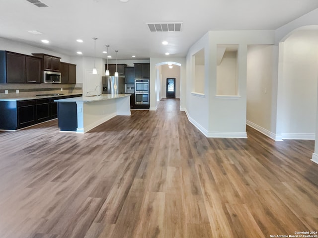 kitchen featuring stainless steel appliances, wood-type flooring, a kitchen island with sink, and pendant lighting