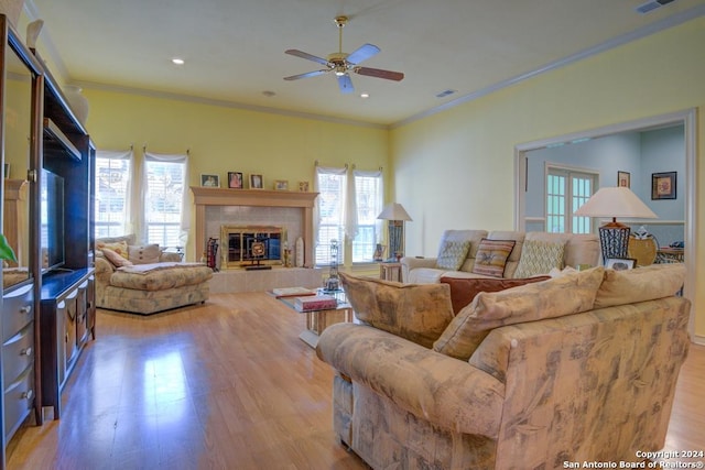 living room featuring a tile fireplace, crown molding, ceiling fan, and wood-type flooring