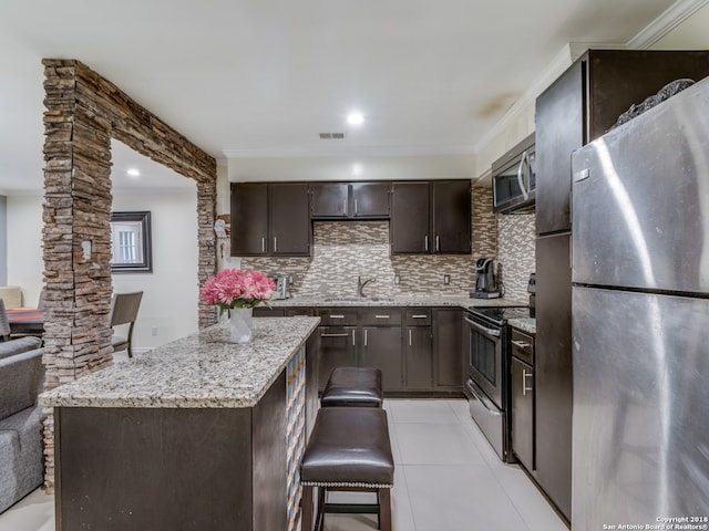 kitchen featuring appliances with stainless steel finishes, tasteful backsplash, dark brown cabinets, sink, and light tile patterned floors