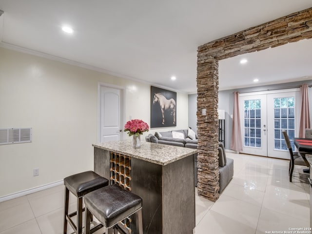 kitchen with light tile patterned flooring, decorative columns, a breakfast bar area, french doors, and light stone counters