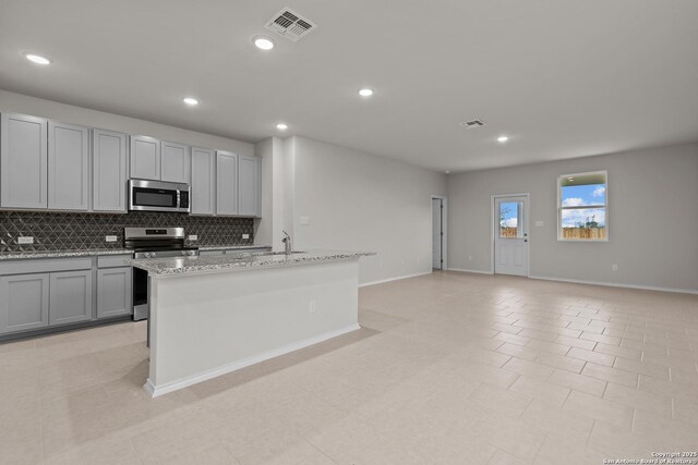 kitchen featuring light wood-type flooring, light stone countertops, sink, appliances with stainless steel finishes, and a center island with sink