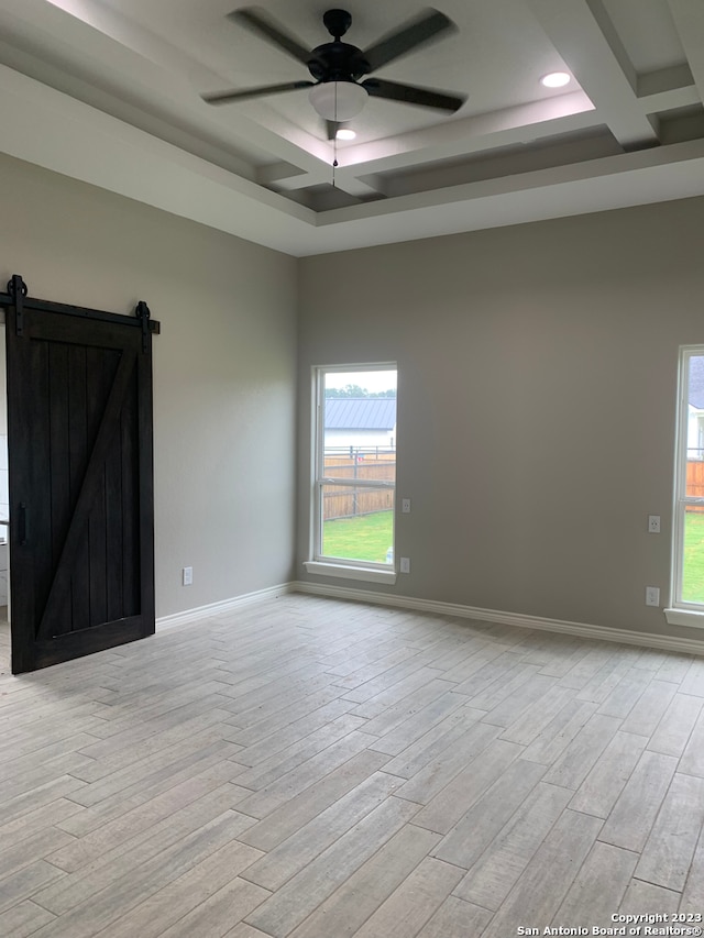 spare room featuring a healthy amount of sunlight, light hardwood / wood-style floors, ceiling fan, and a barn door