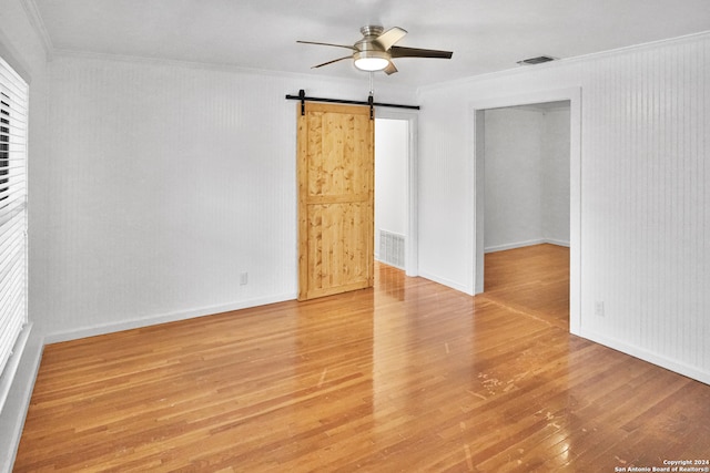 spare room featuring ornamental molding, light hardwood / wood-style flooring, a barn door, and ceiling fan