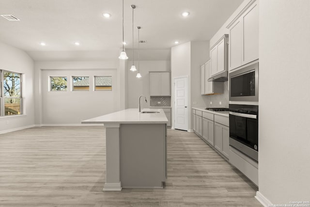 kitchen with decorative light fixtures, an island with sink, sink, backsplash, and stainless steel appliances