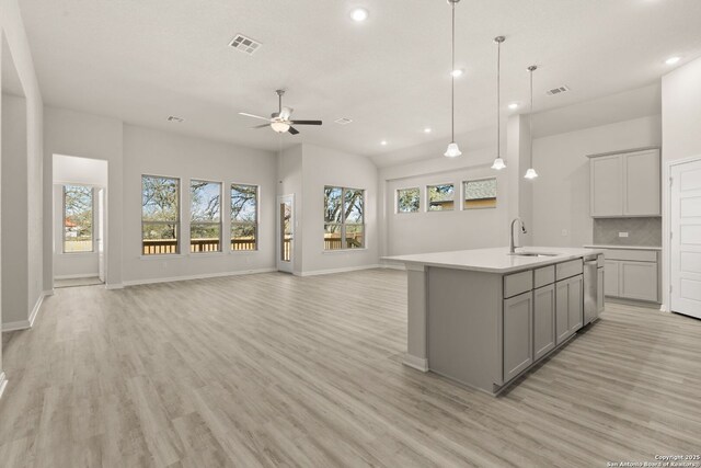 kitchen with sink, a kitchen island with sink, backsplash, gray cabinetry, and hanging light fixtures