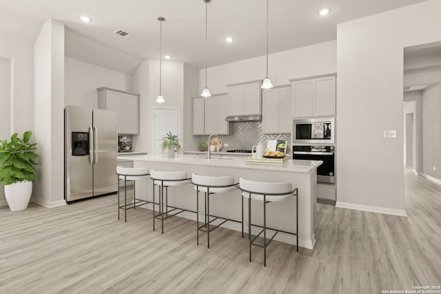 kitchen with a breakfast bar area, decorative backsplash, hanging light fixtures, a kitchen island with sink, and stainless steel appliances