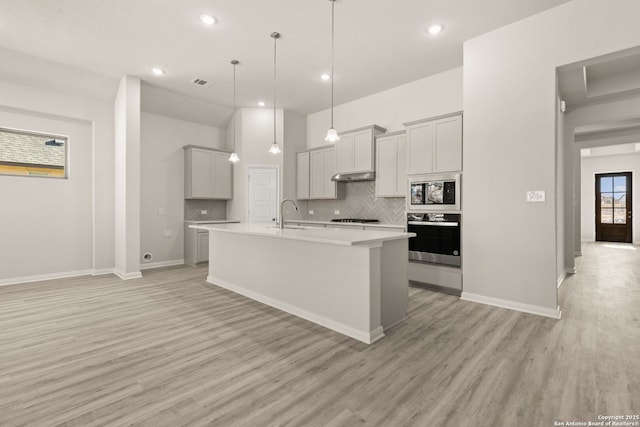 kitchen with built in microwave, decorative light fixtures, light hardwood / wood-style flooring, oven, and a kitchen island with sink