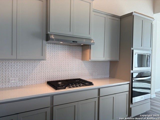 kitchen featuring tasteful backsplash, gray cabinets, stainless steel appliances, and wood-type flooring