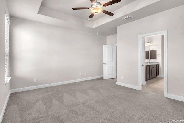 unfurnished bedroom with ceiling fan, light colored carpet, connected bathroom, and a tray ceiling