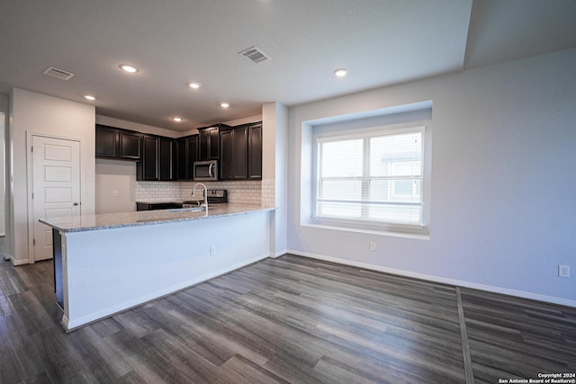 kitchen featuring light stone countertops, appliances with stainless steel finishes, dark wood-type flooring, tasteful backsplash, and kitchen peninsula