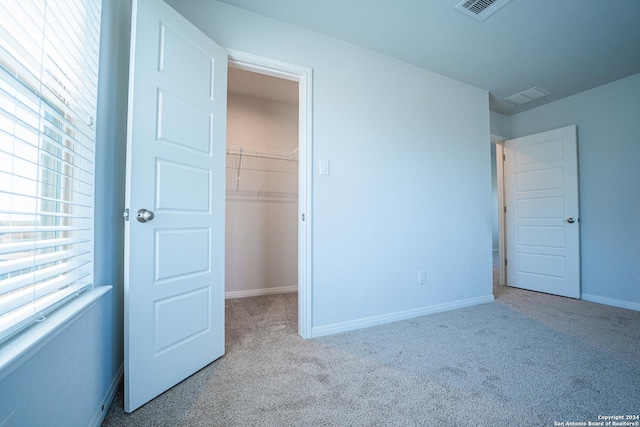 unfurnished bedroom with a spacious closet, a closet, and light carpet