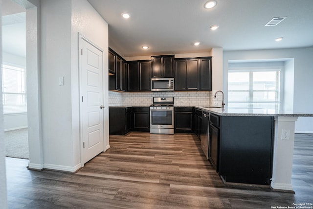 kitchen with stainless steel appliances, decorative backsplash, sink, dark hardwood / wood-style floors, and light stone counters