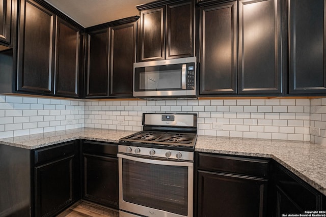 kitchen featuring dark brown cabinets, stainless steel appliances, light stone counters, and backsplash