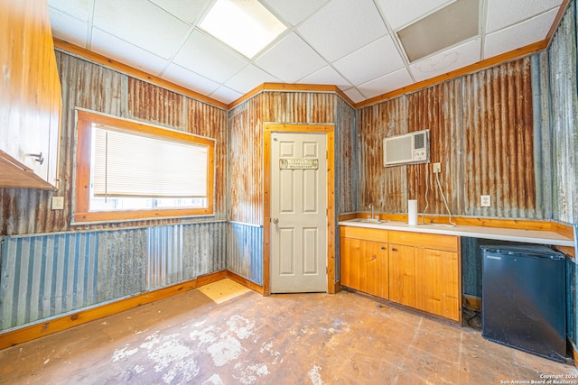 kitchen with a drop ceiling, a wall mounted air conditioner, sink, wood walls, and refrigerator