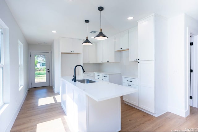 kitchen with white cabinetry, sink, light wood-type flooring, and a center island with sink