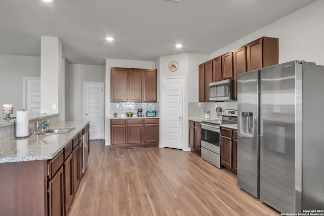 kitchen featuring sink, light hardwood / wood-style flooring, stainless steel appliances, light stone counters, and decorative backsplash