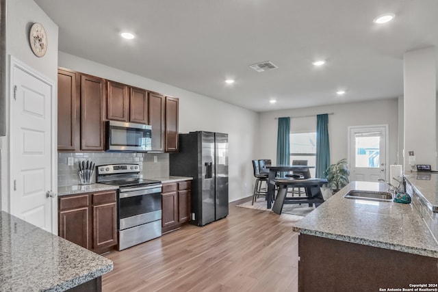 kitchen featuring sink, light wood-type flooring, appliances with stainless steel finishes, light stone countertops, and decorative backsplash