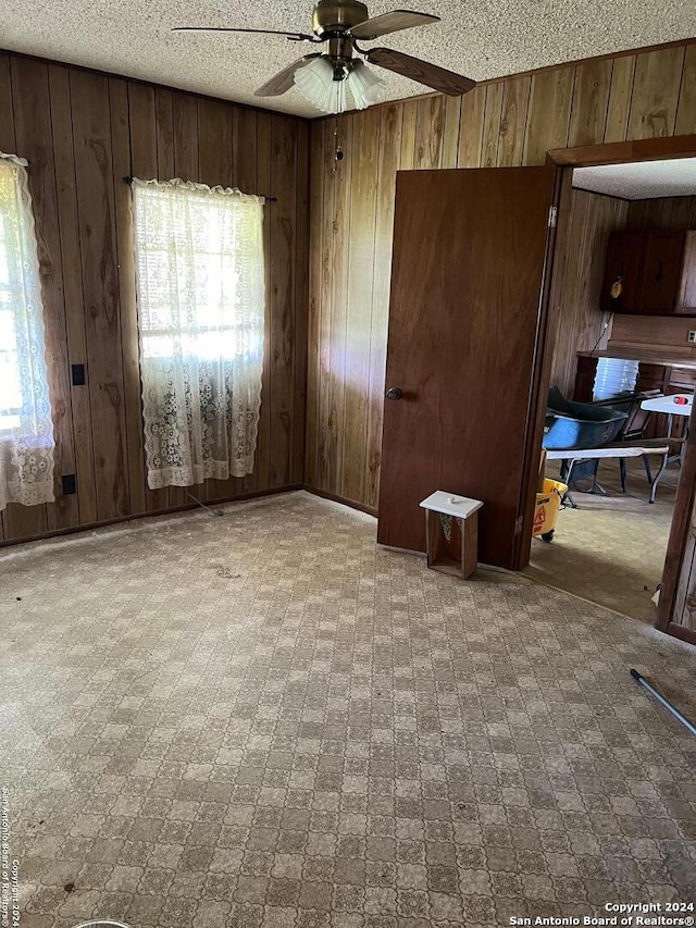 carpeted spare room featuring a textured ceiling, wooden walls, and ceiling fan