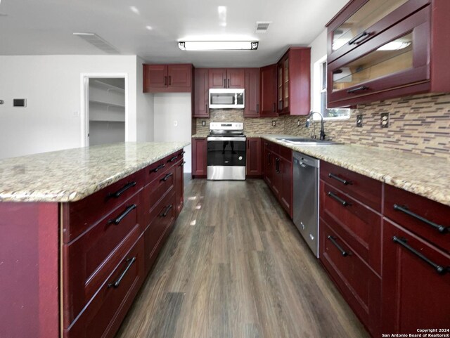 kitchen with stainless steel appliances, sink, backsplash, dark hardwood / wood-style floors, and light stone countertops