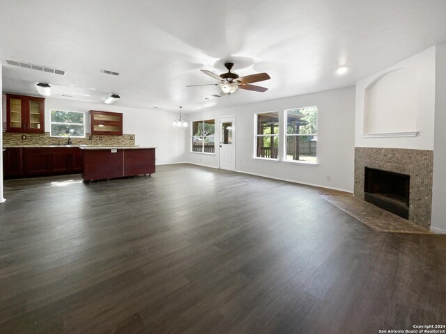 unfurnished living room with sink, dark hardwood / wood-style flooring, a tiled fireplace, and ceiling fan