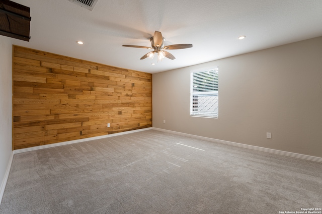 carpeted empty room featuring wood walls and ceiling fan