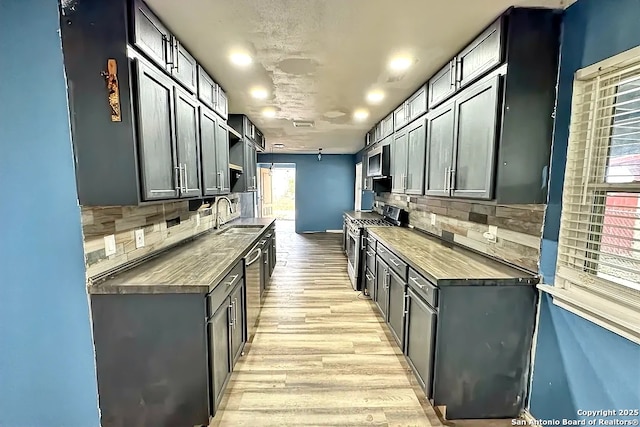 kitchen featuring wood counters, backsplash, stainless steel range with gas cooktop, sink, and light wood-type flooring