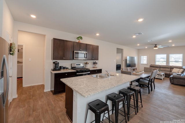 kitchen with sink, a kitchen breakfast bar, a kitchen island with sink, stainless steel appliances, and light hardwood / wood-style flooring