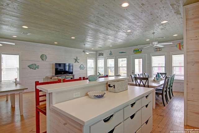 kitchen featuring light hardwood / wood-style flooring, wooden walls, white cabinets, a kitchen island, and ceiling fan