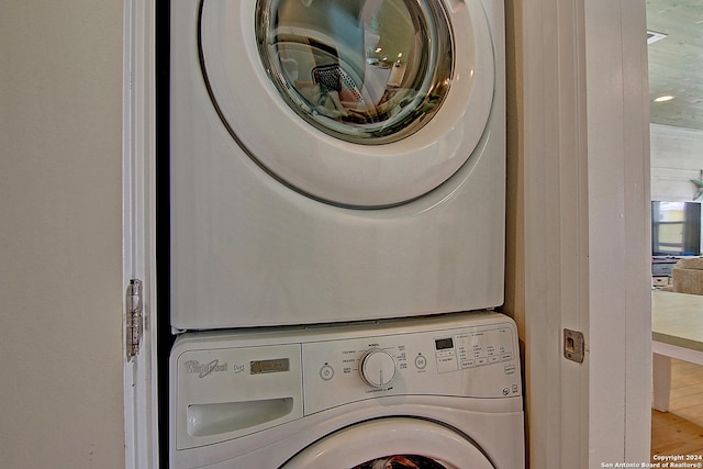 clothes washing area with stacked washer and dryer and wood-type flooring